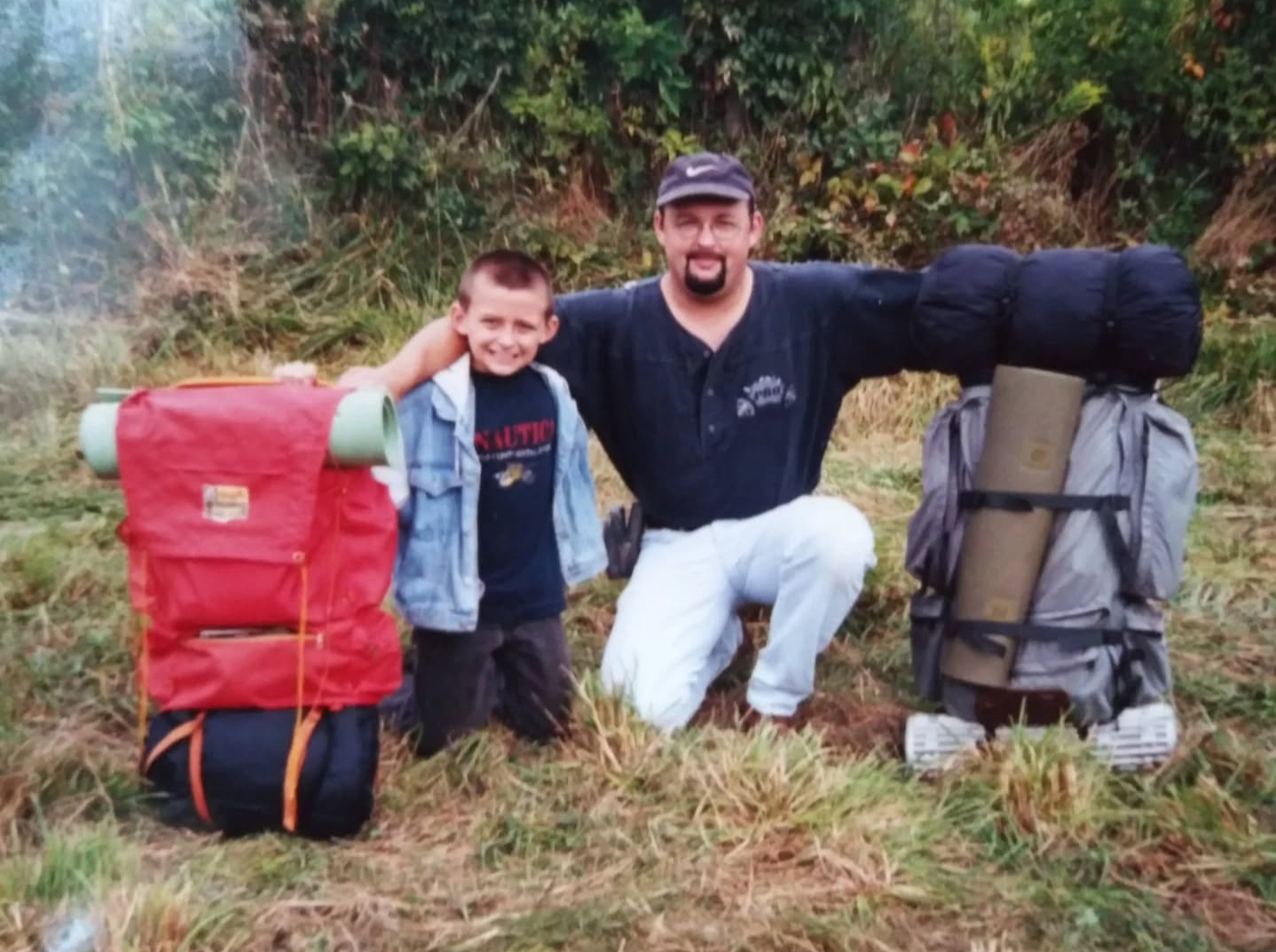 Justin Sovine as a kid, kneeling next to his dad, Chris Sovine, between two loaded backpacks on an early camping trip