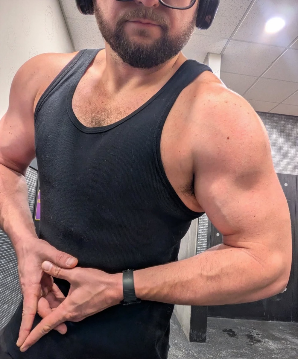 Justin Sovine at the gym in a black tank top, holding a side pose