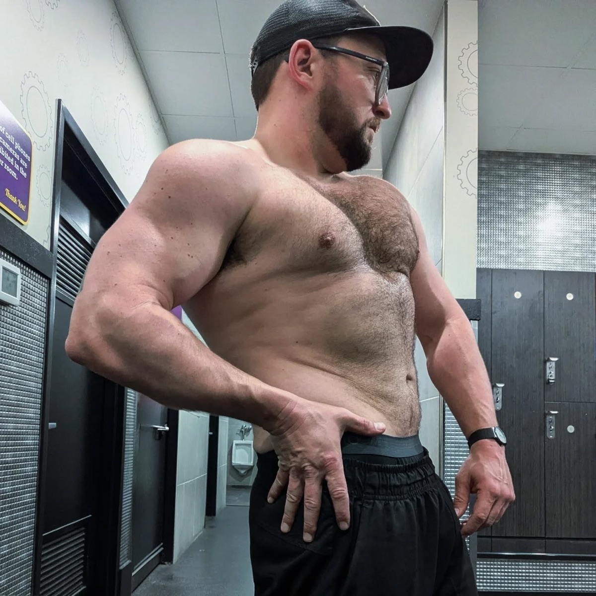 Justin Sovine holding a side chest pose, shirtless, in the gym locker room