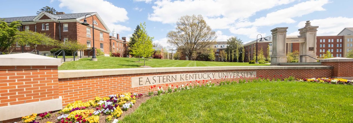 Eastern Kentucky University’s brick entrance wall, with flower beds in front and campus buildings behind