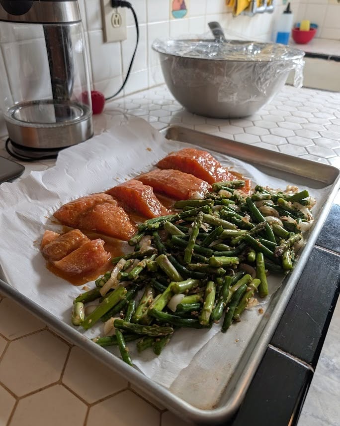 Miso-orange glazed salmon portions and asparagus on a parchment-lined quarter sheet pan on a tile counter